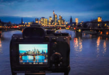 Best Budget Mirrorless Cameras in 2025: Value Testing Guide A full frame mirrorless camera being used on a tripod to capture a long exposure image of Frankfurt's cityscape, with the reflections in the river. The device screen shows the settings to be used - a 13 second exposure at F16, with an ISO of 50.