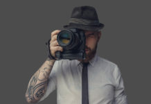 Best Cameras for under $2000 Digital photographer with an expensive digital camera in white shirt and casual hat. Isolated on grey background.