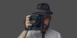 Best Cameras for under $2000 Digital photographer with an expensive digital camera in white shirt and casual hat. Isolated on grey background.