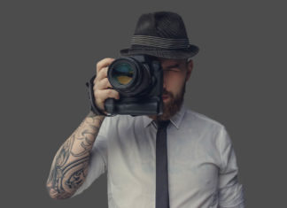 Best Cameras for under $2000 Digital photographer with an expensive digital camera in white shirt and casual hat. Isolated on grey background.