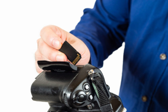 Image contains a man inserting a memory card into his camera.